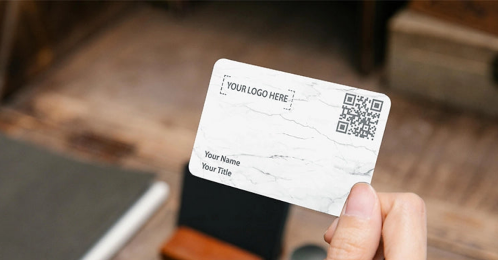 Close-up of a hand holding a marble-textured NFC business card with placeholder logo, name, title, and a QR code for easy contact sharing.
